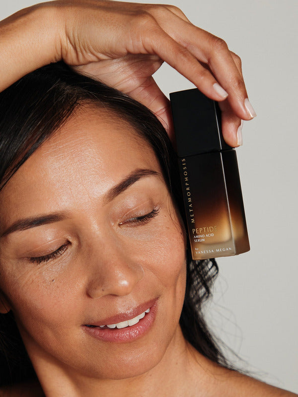 Woman holding Metamorphosis Peptide Amino Acid Serum beside her face with glowing skin.