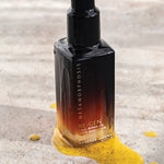 Metamorphosis Re-Gen Cell Repair Oil bottle standing on pale stone beside a textured sweep of golden powder.