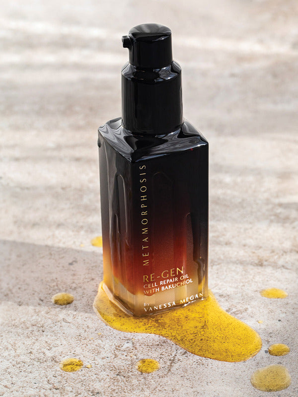 Metamorphosis Re-Gen Cell Repair Oil bottle standing on pale stone beside a textured sweep of golden powder.