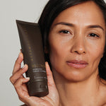 Woman holding a tube of Metamorphosis Recovery Hydrating Cream Cleanser beside her face against a softly lit neutral background.