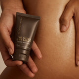 Metamorphosis The Other Lips Balm tube held against bare skin in a warm-toned body care lifestyle photograph.