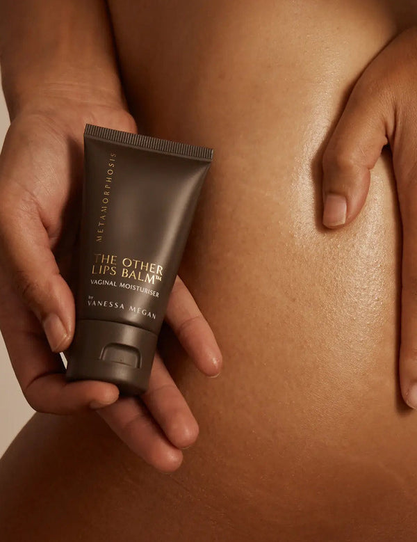 Metamorphosis The Other Lips Balm tube held against bare skin in a warm-toned body care lifestyle photograph.