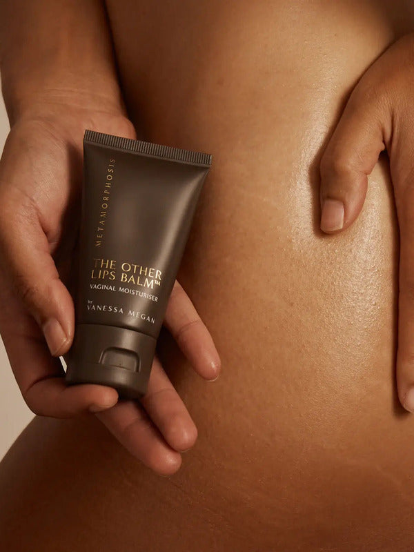 Metamorphosis The Other Lips Balm tube held against bare skin in a warm-toned body care lifestyle photograph.