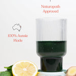 Ribbed glass of dark green Daily Beauty Greens drink with lemon, ginger and green leaves, beneath icons reading Naturopath Approved and 100% Aussie Made.