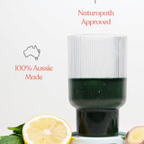 Ribbed glass of dark green Daily Beauty Greens drink with lemon, ginger and green leaves, beneath icons reading Naturopath Approved and 100% Aussie Made.