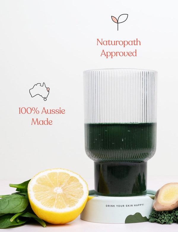 Ribbed glass of dark green Daily Beauty Greens drink with lemon, ginger and green leaves, beneath icons reading Naturopath Approved and 100% Aussie Made.