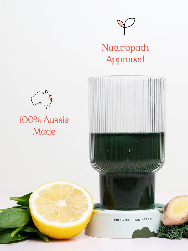 Ribbed glass of dark green Daily Beauty Greens drink with lemon, ginger and green leaves, beneath icons reading Naturopath Approved and 100% Aussie Made.