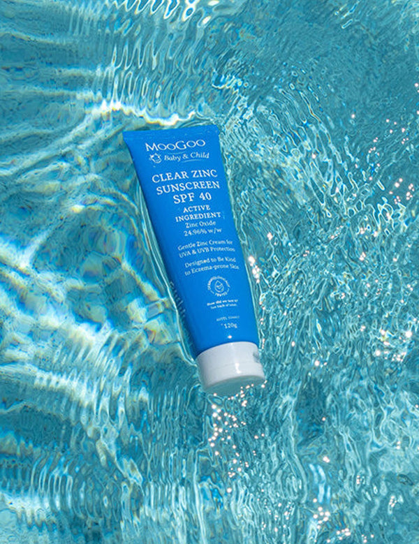 Blue MooGoo Baby Clear Zinc Sunscreen SPF 40 tube floating diagonally in bright rippling pool water.
