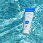 White-and-blue MooGoo Cover Up Buttercup SPF 15 tube floating diagonally in bright blue rippling water.