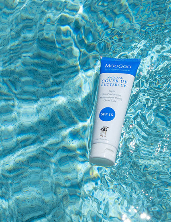White-and-blue MooGoo Cover Up Buttercup SPF 15 tube floating diagonally in bright blue rippling water.