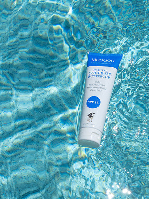 White-and-blue MooGoo Cover Up Buttercup SPF 15 tube floating diagonally in bright blue rippling water.