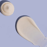 Small rounded dollop and broad smooth smear of off-white MooGoo Double Cream on a lilac background, casting dark shadows.