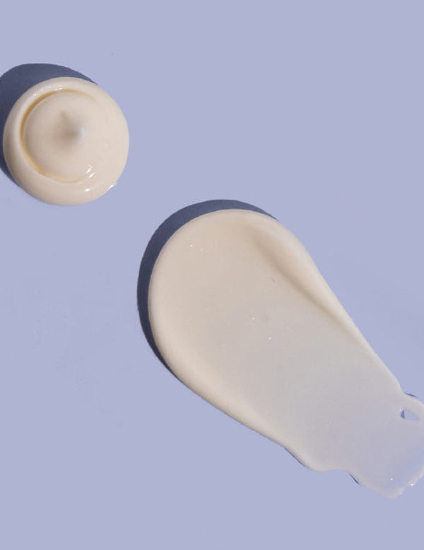 Small rounded dollop and broad smooth smear of off-white MooGoo Double Cream on a lilac background, casting dark shadows.