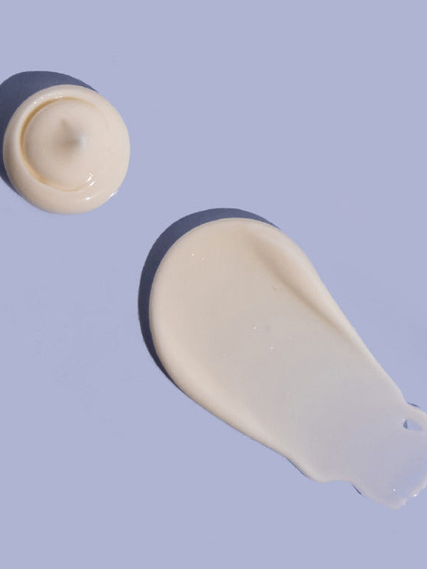 Small rounded dollop and broad smooth smear of off-white MooGoo Double Cream on a lilac background, casting dark shadows.