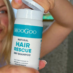 Person opening a white MooGoo Hair Rescue Dry Shampoo bottle held close to the camera, with their face blurred behind it.