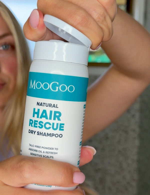 Person opening a white MooGoo Hair Rescue Dry Shampoo bottle held close to the camera, with their face blurred behind it.