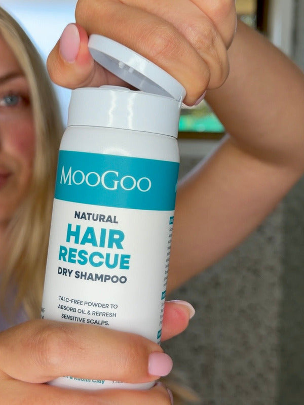 Person opening a white MooGoo Hair Rescue Dry Shampoo bottle held close to the camera, with their face blurred behind it.
