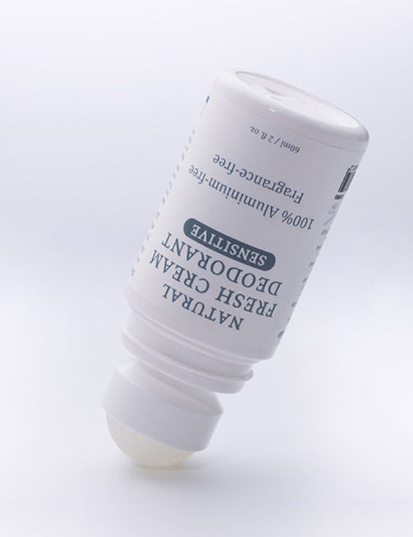 Uncapped MooGoo Natural Fresh Cream Deodorant Fragrance Free bottle tilted with the roller ball resting on a pale surface.