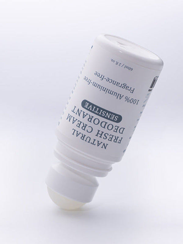 Uncapped MooGoo Natural Fresh Cream Deodorant Fragrance Free bottle tilted with the roller ball resting on a pale surface.
