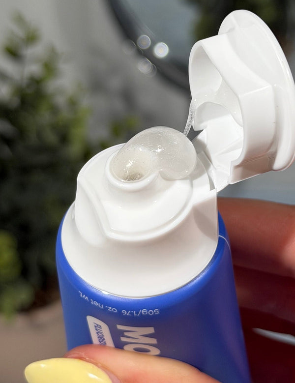 Clear gel toothpaste curling from an open blue MooGoo Kids Blueberry Smoothie Moothpaste tube held in a hand.