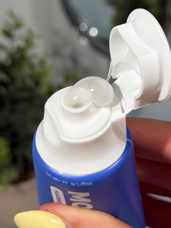 Clear gel toothpaste curling from an open blue MooGoo Kids Blueberry Smoothie Moothpaste tube held in a hand.