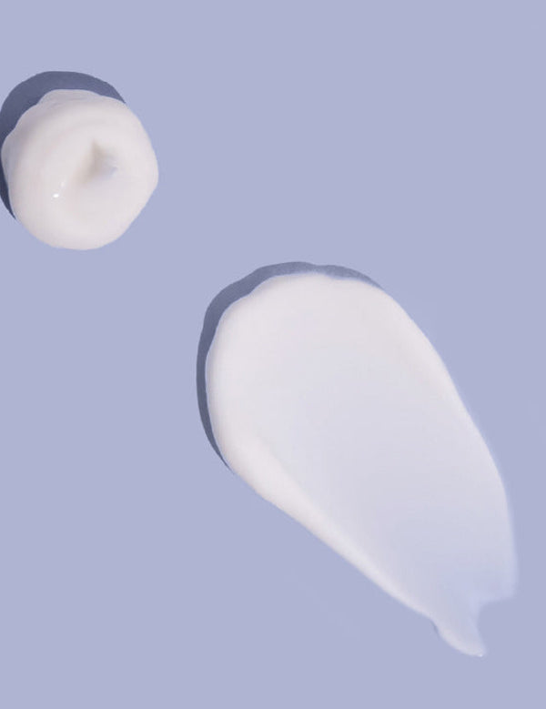Small white dollop and a broad, smooth smear of MooGoo baby lotion on a lilac background, casting shadows along their raised edges.
