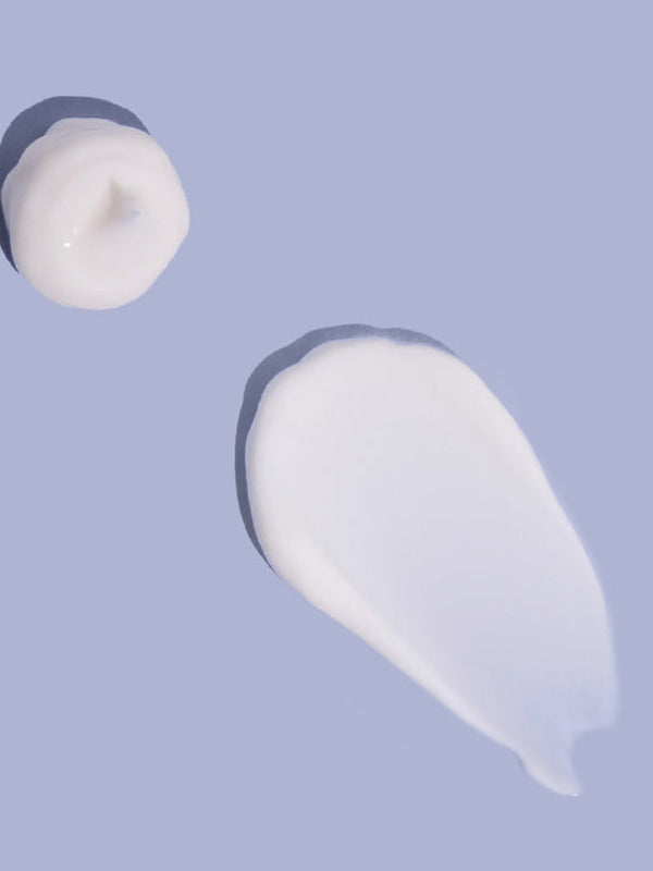 Small white dollop and a broad, smooth smear of MooGoo baby lotion on a lilac background, casting shadows along their raised edges.