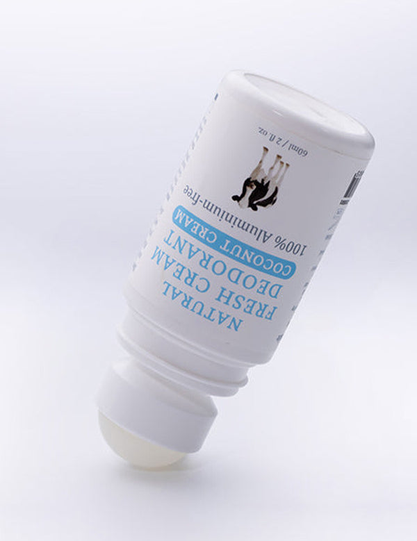 Uncapped white MooGoo Coconut Cream deodorant bottle tilted upside down with its exposed pale roller ball touching the surface.