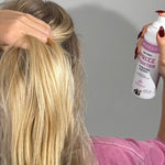 Rear view of a person lifting a section of long blonde hair while aiming a MooGoo Frizz Fighter spray bottle towards it.