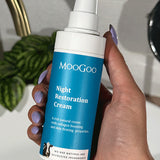 Hand with lilac nail polish holding a blue-labelled MooGoo Night Restoration Cream pump bottle beside a white basin, brass tap and leafy plant.