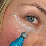 Close-up lifestyle photograph of a woman applying MooGoo 3-in-1 Peptide Eye Serum beneath her eye with the cooling metal roller applicator.
