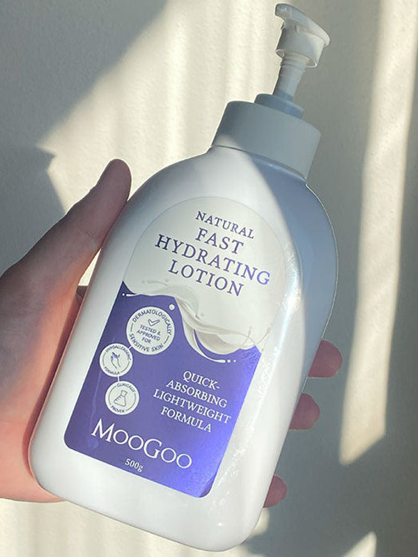 Hand holding a broad white MooGoo Fast Hydrating Lotion pump bottle with a purple label in a bright shaft of sunlight.
