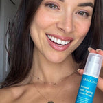 Smiling person holding a blue-labelled MooGoo Retinol Anti-Ageing Active Serum bottle upright beside their face, with its clear cap still on.