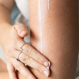 Close-up of a hand rubbing moisturiser into an arm, with a long white streak of cream visible above the hand.