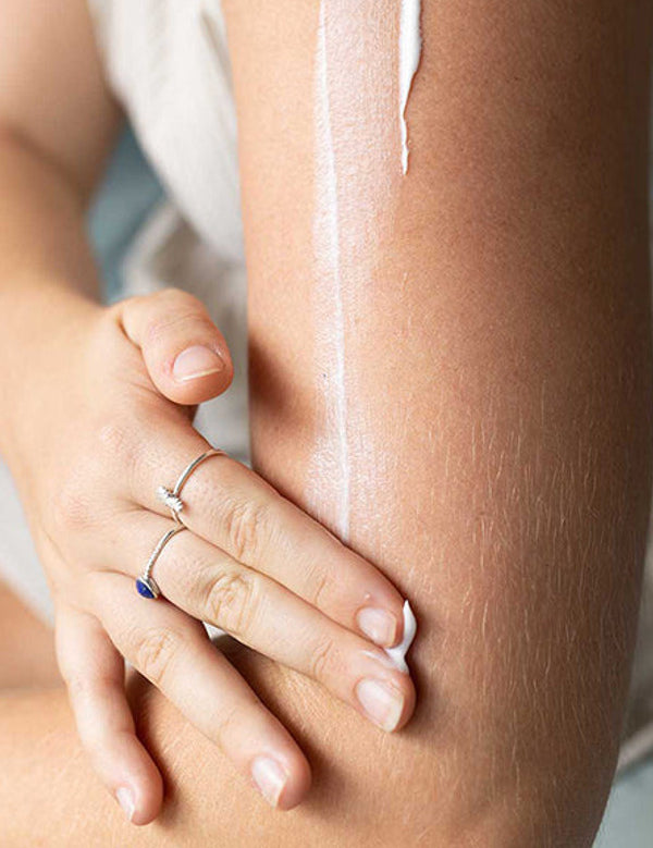 Close-up of a hand rubbing moisturiser into an arm, with a long white streak of cream visible above the hand.