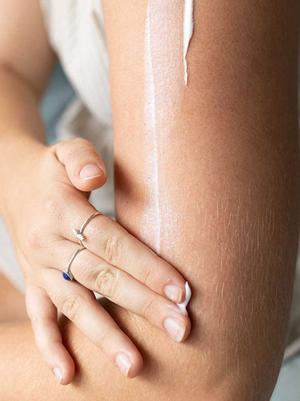 Close-up of a hand rubbing moisturiser into an arm, with a long white streak of cream visible above the hand.
