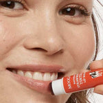 Smiling woman holding MooGoo Strawberry Tinted Lip Balm beside her lips, showing the warm red tint.