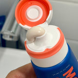 Close-up of an open MooGoo Watermelon and Mint Moothpaste tube with toothpaste visible at the orange flip-cap nozzle.