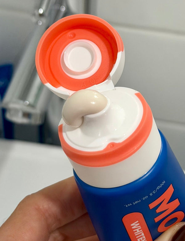 Close-up of an open MooGoo Watermelon and Mint Moothpaste tube with toothpaste visible at the orange flip-cap nozzle.