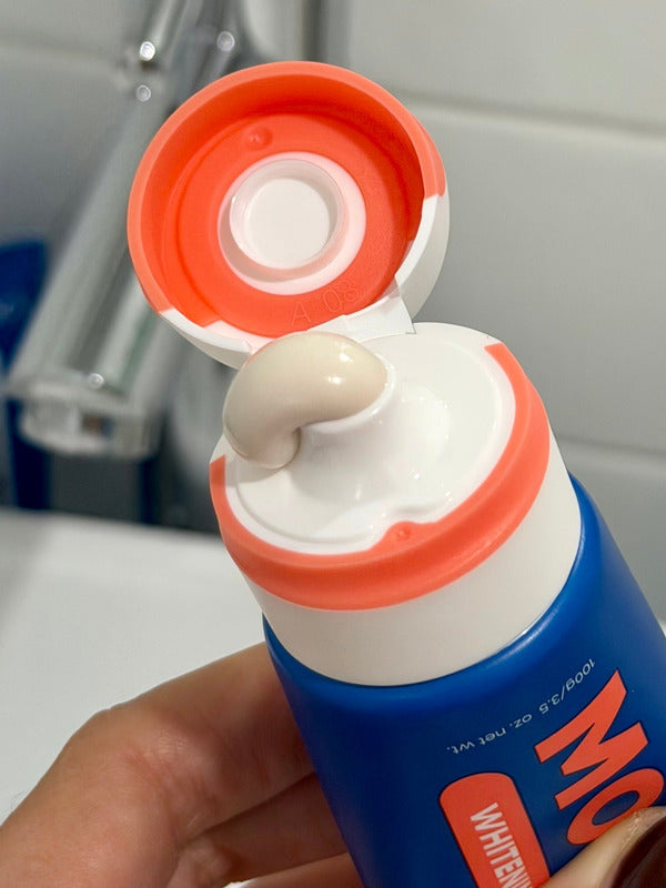 Close-up of an open MooGoo Watermelon and Mint Moothpaste tube with toothpaste visible at the orange flip-cap nozzle.