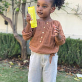 Child holding MOTHER SPF Face and Body sunscreen outdoors