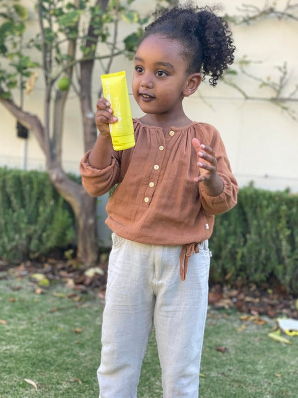 Child holding MOTHER SPF Face and Body sunscreen outdoors