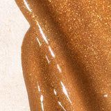 Mukti Golden Glow Bronzing Drops serum swatch showing its glossy bronze colour and fine golden shimmer on a pale textured surface, labelled Golden Glow.