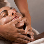 Reclining person receiving a gentle facial cleanse and massage with the Mukti Luxe Bamboo Facial Cleansing Mitt.