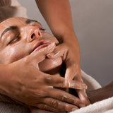 Reclining person receiving a gentle facial cleanse and massage with the Mukti Luxe Bamboo Facial Cleansing Mitt.