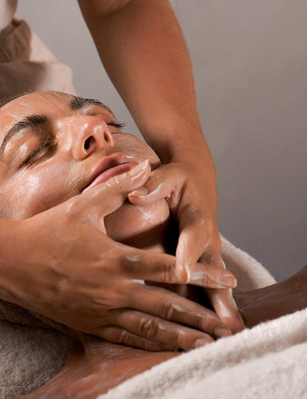 Reclining person receiving a gentle facial cleanse and massage with the Mukti Luxe Bamboo Facial Cleansing Mitt.