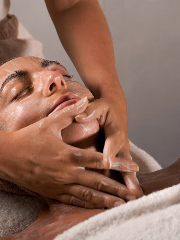 Reclining person receiving a gentle facial cleanse and massage with the Mukti Luxe Bamboo Facial Cleansing Mitt.