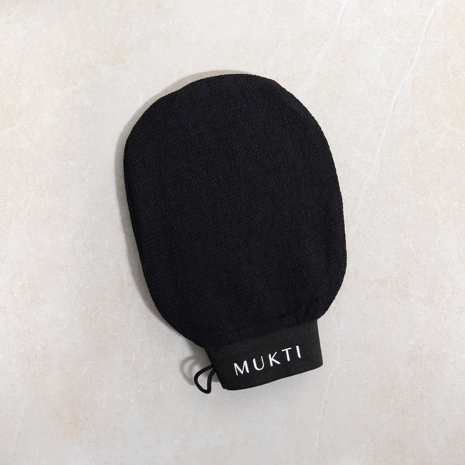 Mukti Body Exfoliating Mitt styled on a warm stone surface