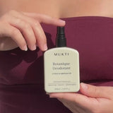 Person wearing a plum top holding Mukti Botanique Natural Deodorant Citrus & Siberian Fir against their torso.