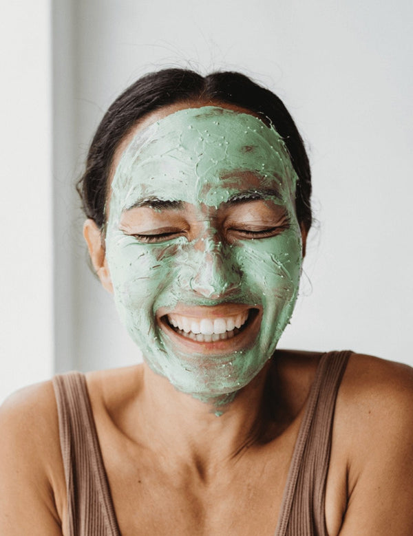 Smiling woman wearing a green layer of Mukti Deep Cleanse Enzyme Mask across her face.